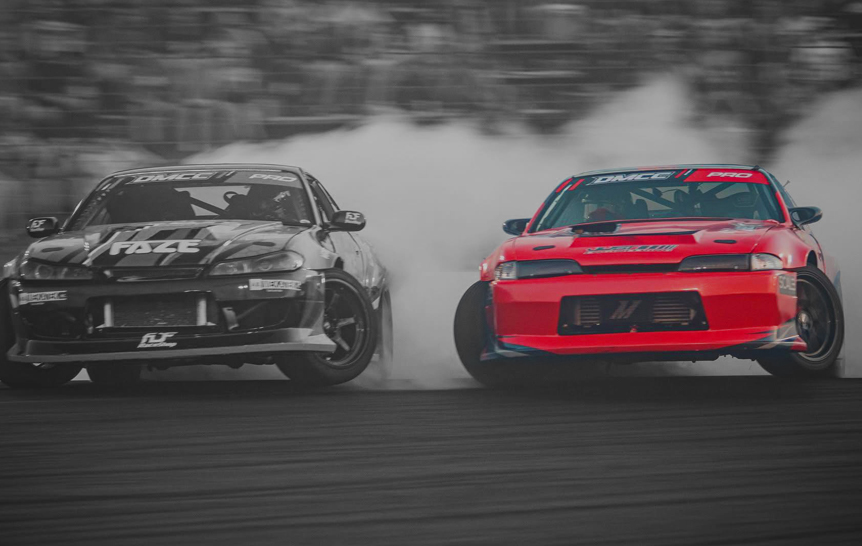 Two drift cars driving in tandem at a motorsports facility